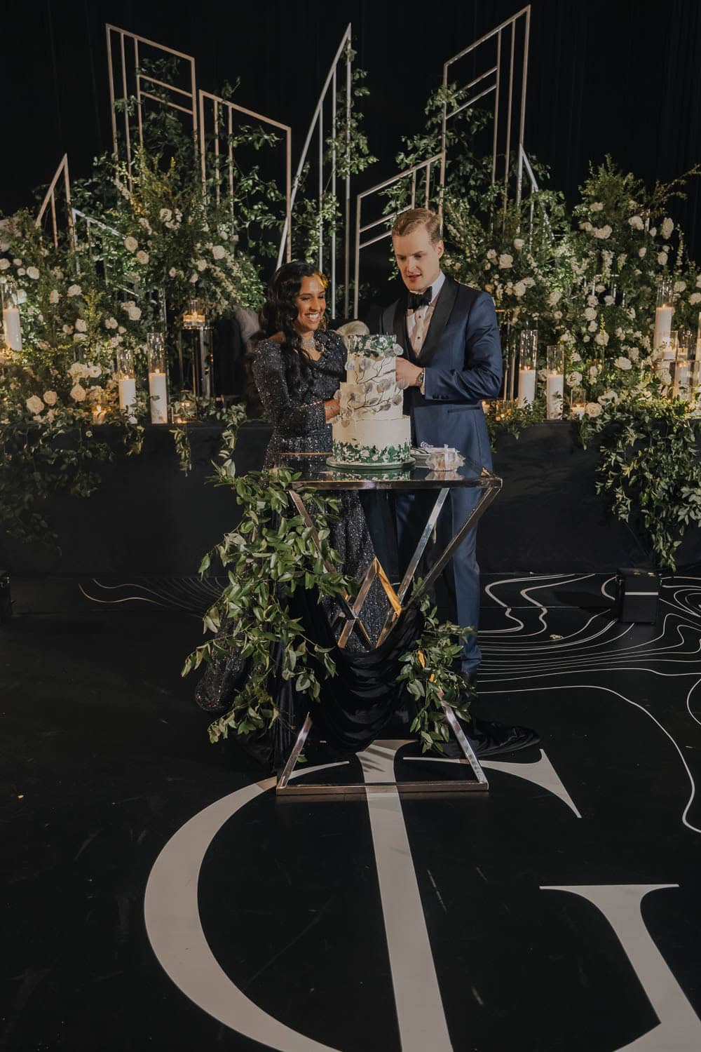 Wedding couple cutting the cake in a beautifully decorated venue with lush greenery and floral arran.